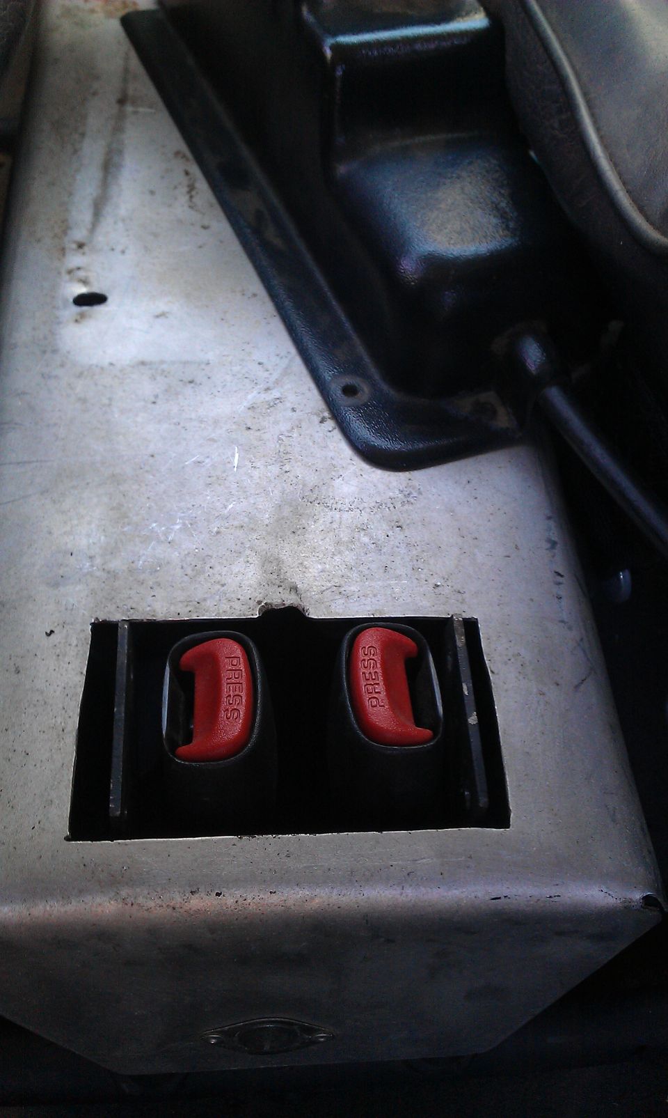 Two red seat belt buckles with 'PRESS' visible, set into a metal panel