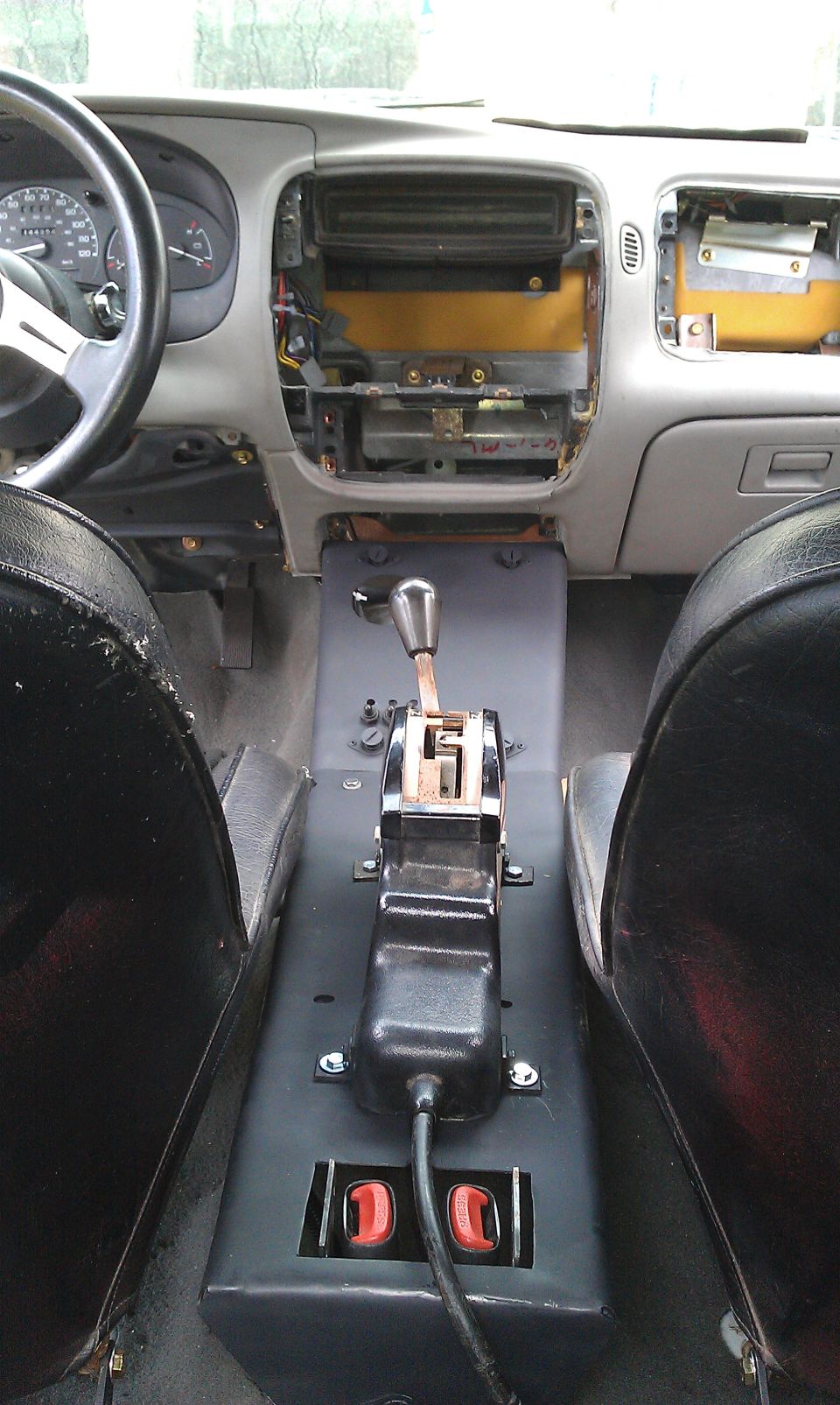 Interior shot of a vehicle with dashboard removed, showing exposed wiring and center console with shifter