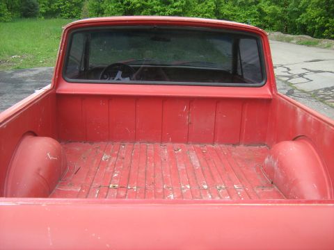 1964 Ford Ranchero - The worn wooden floor of a red pickup truck's bed is visible, with the interior and steering wheel seen through the back window.