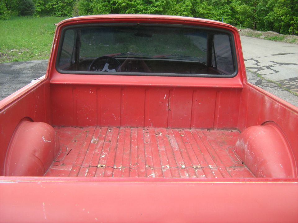 Red pickup truck bed, showing the floor and sides. Steering wheel visible through the rear window