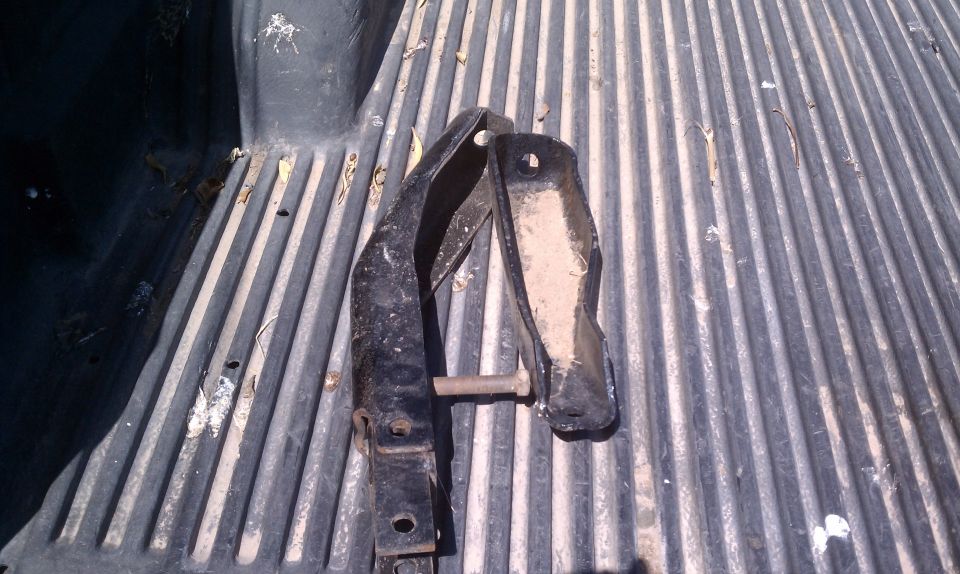 Two metal brackets with a bolt, resting on a ribbed truck bed