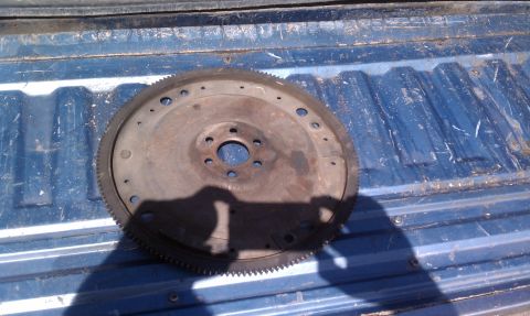 1979 Ford Bronco - A used flywheel rests on the blue, ribbed surface of a truck bed under bright sunlight.