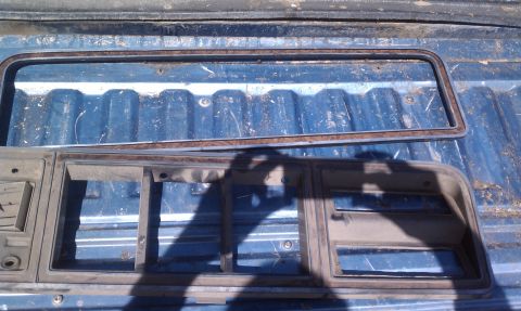 1979 Ford Bronco - Two trim pieces, likely for a vehicle's grille and window, rest on a blue truck bed.