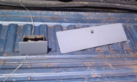1979 Ford Bronco - Gray ashtray and cover are shown removed from a vehicle bed, with visible wiring.