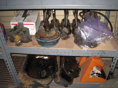 1979 Ford Bronco - Various engine components are organized on shelves, some in plastic bags, alongside other automotive parts.