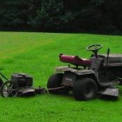 1989 Ford Bronco - A riding mower pulls a trailer with a push mower across a green lawn.