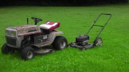 1989 Ford Bronco - Two mowers sit on a grassy lawn, one a riding mower and the other a push mower.