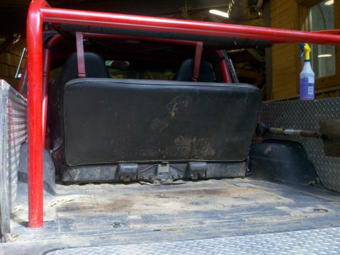 1979 Ford Bronco - The rear interior of a vehicle shows a bench seat and a red roll cage, with diamond plate accents in the cargo area.