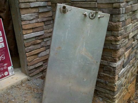 1979 Ford Bronco - A large metal tank with fittings is leaning against a stone wall.