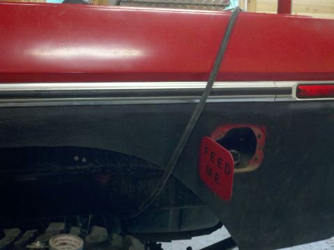1979 Ford Bronco - Close-up of a red vehicle's rear quarter panel, showing a black fender flare and an open fuel door with a 'FEED ME' sticker.