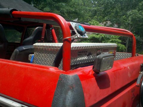 1979 Ford Bronco - Interior view of a red off-road vehicle, equipped with a roll cage and a toolbox.