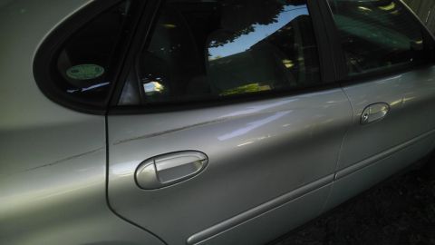 1989 Ford Bronco - The side profile of a silver sedan shows its rear door and window, with reflections on the glass.