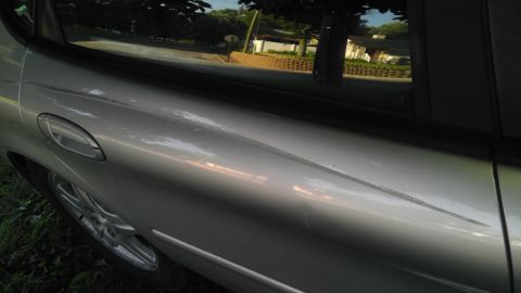 1989 Ford Bronco - A side view of a silver car shows a prominent scratch along the door panel.