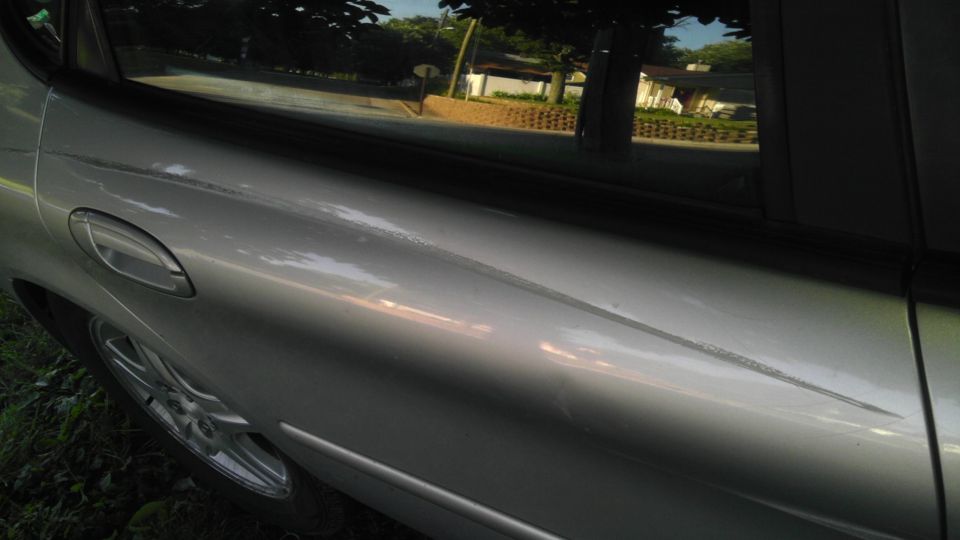 Silver car door with a long scratch and a visible door handle