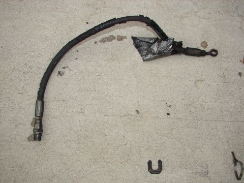 1992 Ford Taurus - A damaged brake hose with a metal fitting on one end and a loop on the other, resting on a concrete surface.