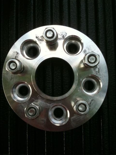 1993 Ford Crown Victoria - A silver wheel spacer with eight lug nut holes is shown against a dark, ribbed background.