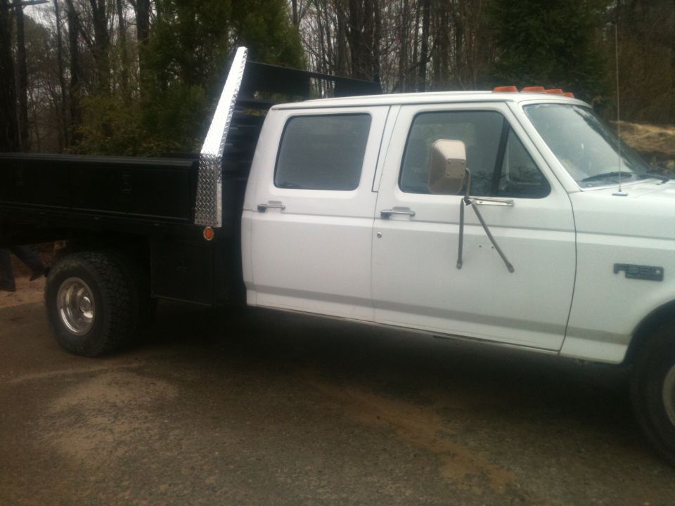 White crew cab flatbed truck, side view. Looks like a 1990s Ford F-Series