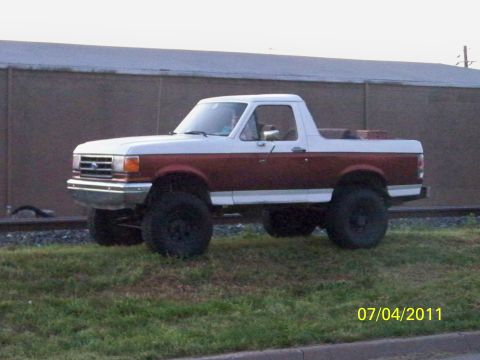 1989 Ford Bronco - A lifted 1989 Ford Bronco is parked on grassy terrain next to railroad tracks.
