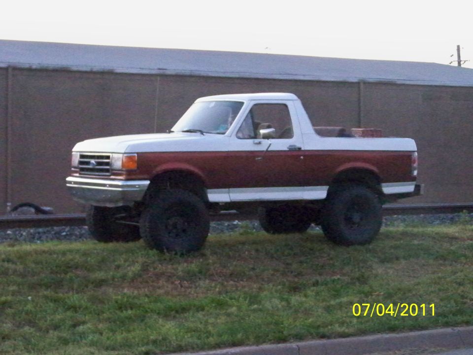Two-tone red and white Ford Bronco with lifted suspension and large tires, viewed from the side
