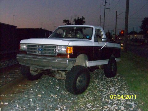 1989 Ford Bronco - Two-tone 1989 Ford Bronco sits on railroad tracks as twilight settles.