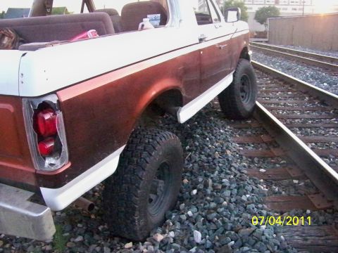 1989 Ford Bronco - Rear view of a 1989 Ford Bronco with a damaged taillight, positioned on railroad tracks.