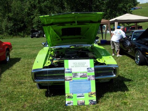 1975 Ford Ranchero - A lime green 1973 Dodge Charger SE Brougham is displayed with its hood open, alongside a display board detailing its features.