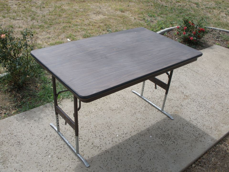 Folding table with dark woodgrain top and adjustable steel legs on a concrete patio