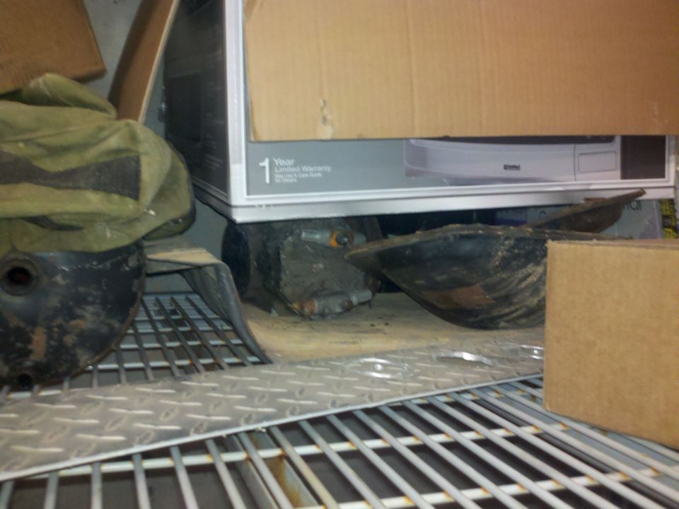Vehicle parts, including a black housing and metal components, stored on shelves with cardboard boxes