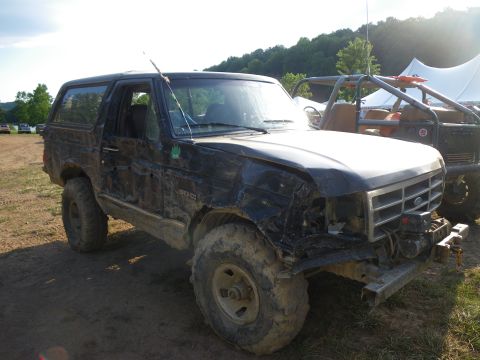 1995 Ford Bronco - This heavily damaged Ford Bronco is seen off-road, with another vehicle and a tent in the background.