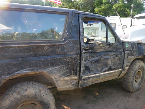 1995 Ford Bronco - This heavily damaged black Ford Bronco, identified as a 1995 model, shows extensive dents and mud splatter.