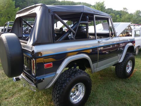 1995 Ford Bronco - This two-tone blue and silver Ford Bronco features a soft top, roll cage, and a spare tire mounted on the rear.
