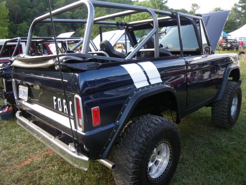 1995 Ford Bronco - This modified Ford Bronco features a prominent roll cage and racing stripes, parked outdoors with other vehicles.