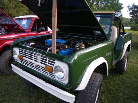 1995 Ford Bronco - A green 1970s Ford Bronco is displayed with its hood open, parked next to a red vehicle.