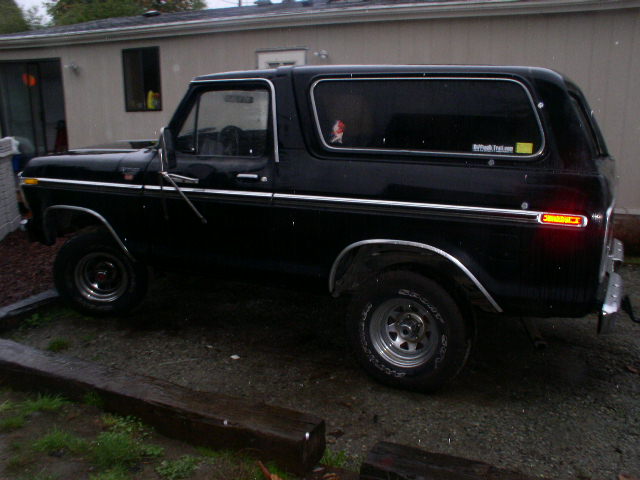Black Ford Bronco SUV in side profile parked on gravel by a beige building