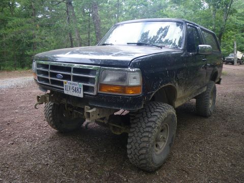 1995 Ford Bronco - This lifted Ford Bronco is parked off-road, with another vehicle visible in the background.