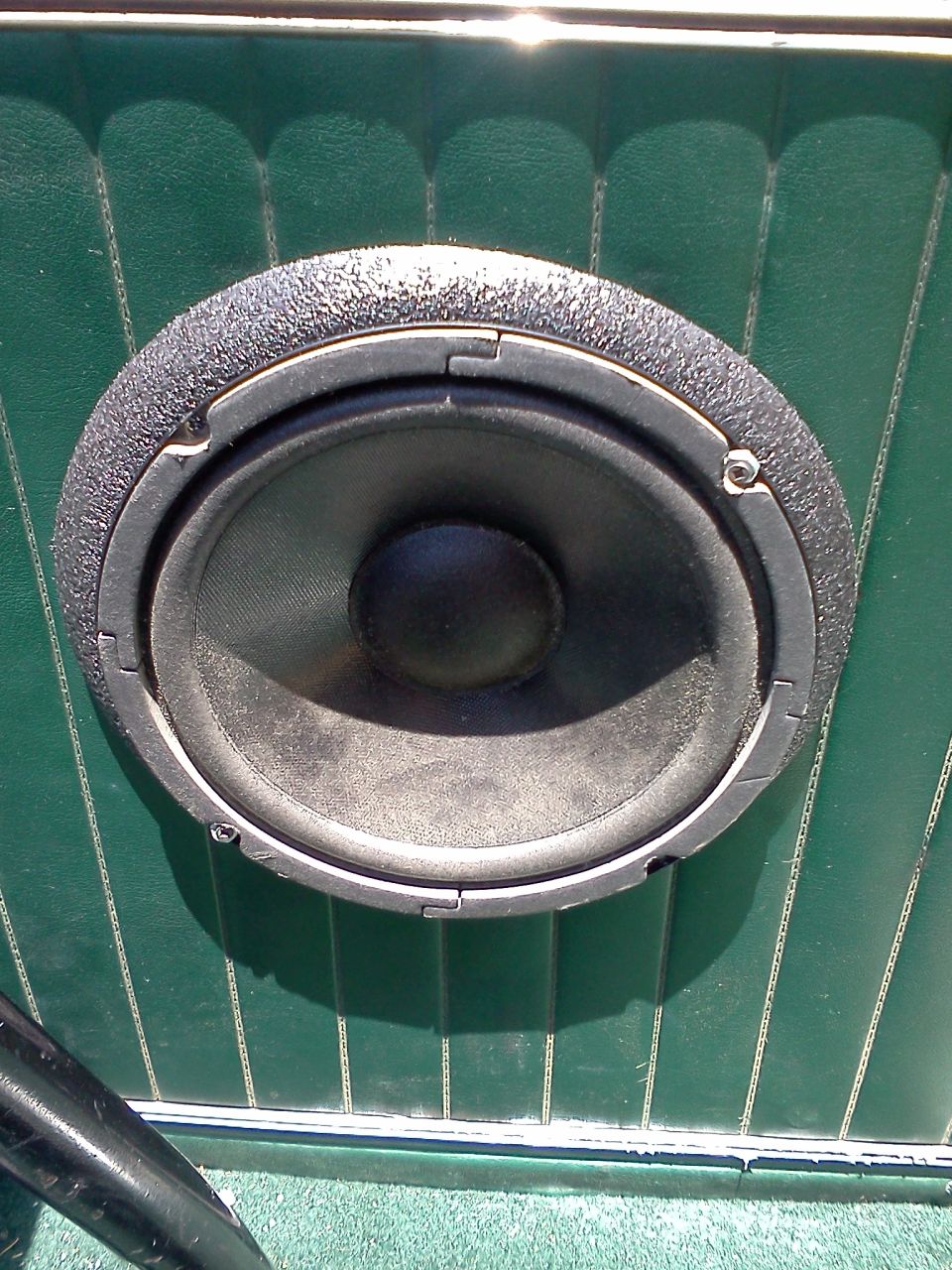 close-up of a round speaker mounted in a green door panel with vertical stitching