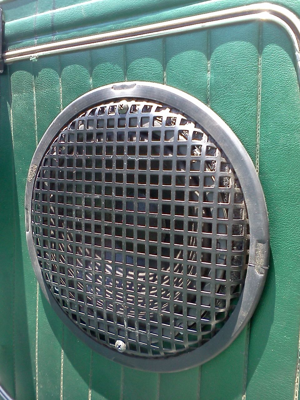Round speaker grille with black squares on a green textured vehicle door panel