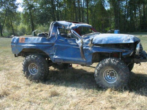1979 Ford Bronco - This blue truck has significant damage to its body and roof, with large off-road tires.