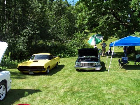 1975 Ford Ranchero - Two vehicles are parked on a grassy field under trees, with people gathered nearby.