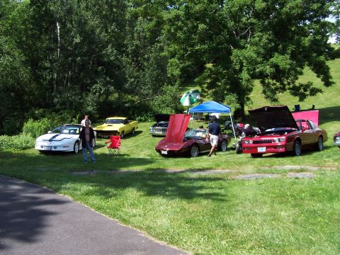 1975 Ford Ranchero - Several classic cars are displayed on a grassy field under trees, with tents set up in the background.