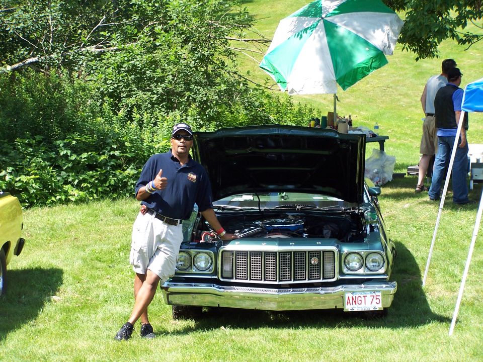 Dark green 1970s Ford Ranchero with hood up at a car show, man giving thumbs-up
