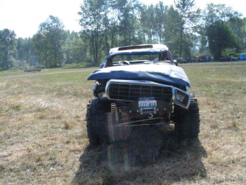 1979 Ford Bronco - A heavily damaged blue off-road vehicle sits in a grassy field.