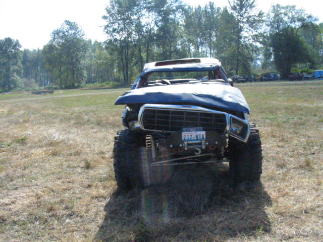 Lifted doorless Ford 4x4 with roll cage, mud tires and front winch in a grass field