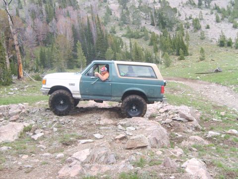 1989 Ford Bronco - 1989 Ford Bronco navigating a rocky mountain trail with trees and hills in the background.