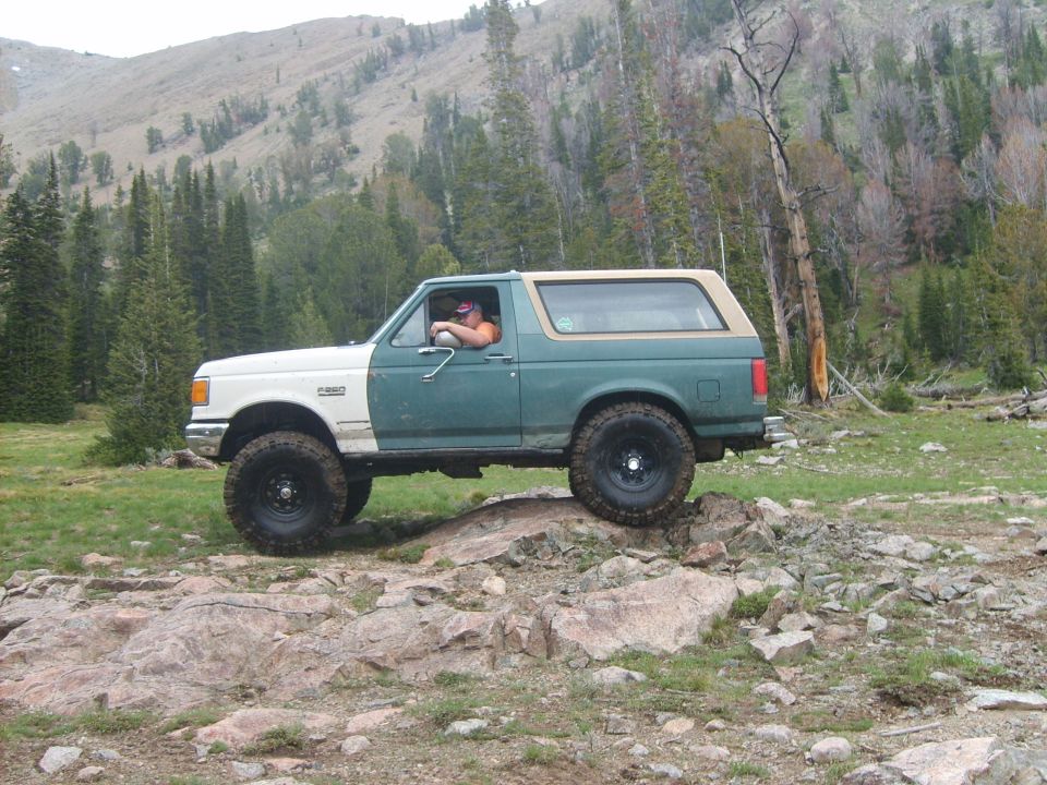 Ford Bronco driving over rocks on a trail, driver visible