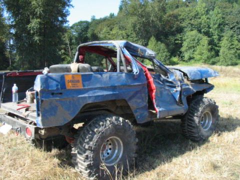1979 Ford Bronco - This heavily modified 1979 Ford Bronco features a roll cage and large off-road tires, showing significant damage.