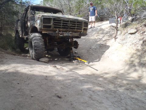 1979 Ford Bronco - This heavily modified 1979 Ford Bronco, with oversized tires and a jack under its front end, navigates a challenging off-road terrain.