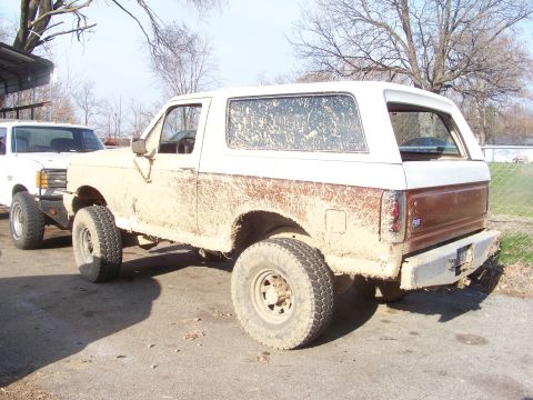 1989 Ford Bronco - A muddy 1989 Ford Bronco is parked next to a white pickup truck.