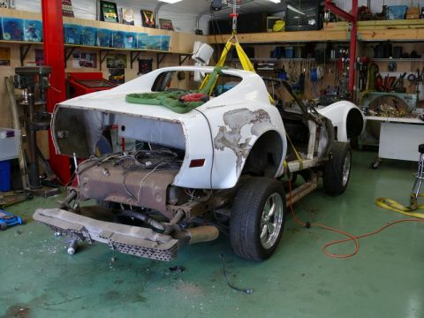 1976 Chevrolet Corvette - A white car body, likely a 1975 model, is being lifted in a workshop. The vehicle is in a state of disrepair, with significant rust and mis…