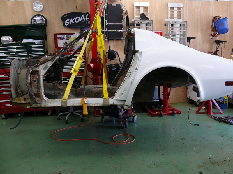 White car body on repair stands, lifted by yellow straps, showing disassembled interior and rear quarter panel